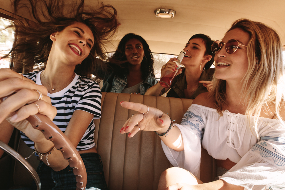 4 women sit in a car, smiling during their girls trip to New Orleans.